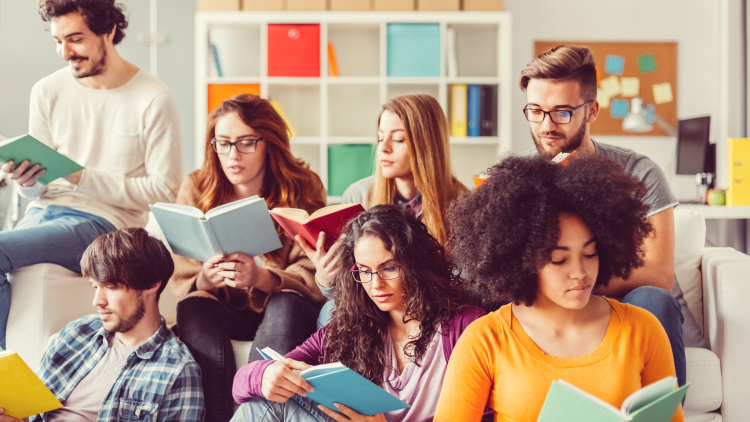 A group of peers sit in a classroom reading books individually.